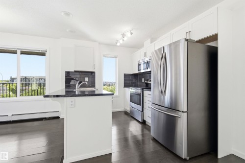 Kitchen featuring white cabinetry, stainless steel appliances, dark countertops, a dark tile backsplash, and dark wood-finish flooring - 435 5515 7 Avenue, Edmonton, AB 