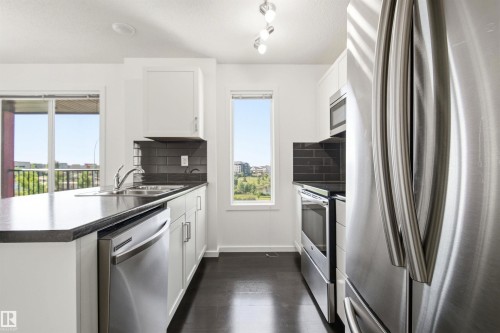 Modern kitchen featuring stainless steel appliances, dark wood-finish flooring, white cabinetry, dark subway tile backsplash, and dark countertops - 435 5515 7 Avenue, Edmonton, AB 
