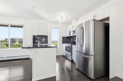Kitchen featuring white cabinetry, stainless steel appliances, dark countertops, a dark tile backsplash, and dark wood-finish flooring - 