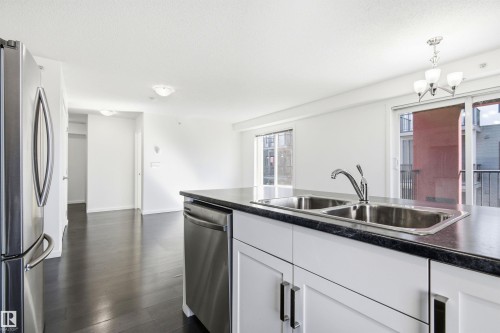 Kitchen island featuring a double-basin stainless steel sink with a single-handle faucet, integrated stainless steel dishwasher, and dark countertop - 435 5515 7 Avenue, Edmonton, AB 