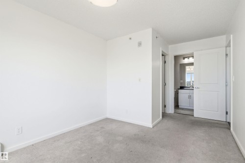 Carpeted room featuring a white ceiling and baseboards, with a bathroom entrance revealing a vanity with a dark countertop and mirror - 435 5515 7 Avenue, Edmonton, AB 