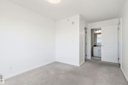 Carpeted room featuring a white ceiling and baseboards, with a bathroom entrance revealing a vanity with a dark countertop and mirror - 