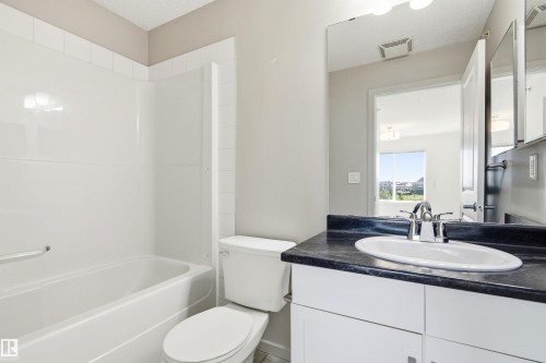 Bathroom featuring a bathtub with integrated shower, single vanity with a dark countertop and undermount sink, and chrome fixtures - 435 5515 7 Avenue, Edmonton, AB 