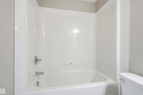 White bathtub with integrated shower surround, chrome fixtures, and coordinating white tile trim - 435 5515 7 Avenue, Edmonton, AB 