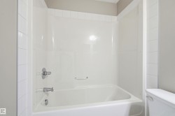 White bathtub with integrated shower surround, chrome fixtures, and coordinating white tile trim - 