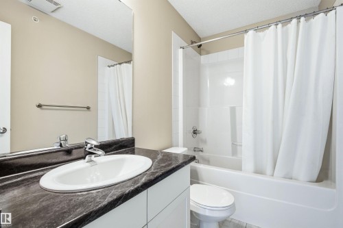 Bathroom featuring a dark-toned countertop with an integrated white sink, chrome faucet, and a large wall-mounted mirror - 435 5515 7 Avenue, Edmonton, AB 