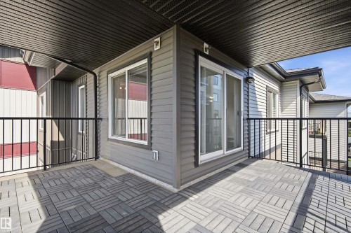 Spacious outdoor balcony featuring patterned paving, dark metal railings, and a dark soffit ceiling - 435 5515 7 Avenue, Edmonton, AB 