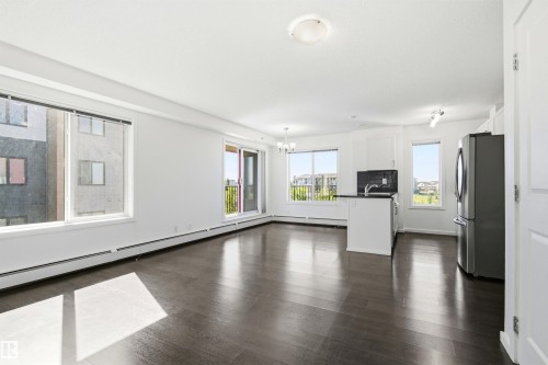 Open-concept living space featuring dark wood-finish flooring, white walls, and multiple windows for natural illumination - 435 5515 7 Avenue, Edmonton, AB 