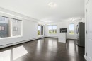 Open-concept living space featuring dark wood-finish flooring, white walls, and multiple windows for natural illumination - 435 5515 7 Avenue, Edmonton, AB 