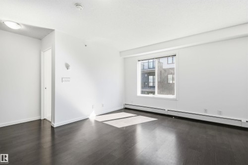 Spacious room featuring dark wood-finish flooring, white walls, and a large window with white trim - 435 5515 7 Avenue, Edmonton, AB 