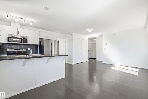 Open concept living space featuring wood-finish flooring, a kitchen island with stone countertop, white cabinetry with stainless steel appliances, and track lighting - 435 5515 7 Avenue, Edmonton, AB 