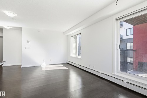 Spacious room featuring dark wood-finish flooring, white walls, and a large sliding glass door with balcony access - 435 5515 7 Avenue, Edmonton, AB 
