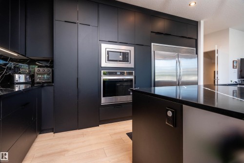 Modern kitchen featuring matte black cabinetry, integrated stainless steel appliances, black countertops, and a complementary black marble-effect backsplash - 4714 Charles Bay Bay, Edmonton, AB 