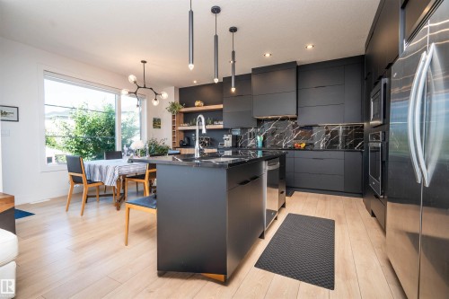 Modern kitchen featuring dark cabinetry, dark countertops, and a black marble-patterned backsplash - 4714 Charles Bay Bay, Edmonton, AB 