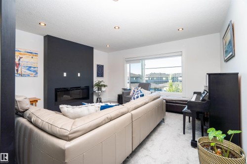 Living area featuring a modern black accent wall with an integrated linear fireplace, recessed ceiling lighting, a large window, and light-toned carpet flooring - 4714 Charles Bay Bay, Edmonton, AB 