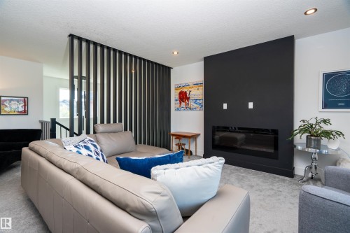 Living area featuring an accent wall with a built-in electric fireplace and light gray carpet flooring - 4714 Charles Bay Bay, Edmonton, AB 