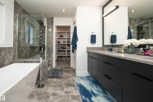 Contemporary bathroom featuring a freestanding tub, glass-enclosed shower with multiple sprayers, and a long double vanity with dark cabinetry - 4714 Charles Bay Bay, Edmonton, AB 