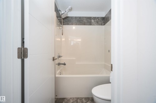 Full bathroom featuring a white tub-shower combination with a dark gray tiled surround and a coordinating gray stone-finish floor - 4714 Charles Bay Bay, Edmonton, AB 
