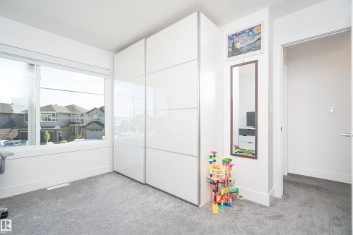 Bright room featuring a large window, light gray carpet, and white built-in cabinetry with sliding doors - 4714 Charles Bay Bay, Edmonton, AB 