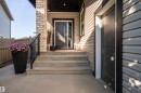 Contemporary entryway featuring light brickwork, grey siding, concrete stairs, and a dark wood-finish front door with a vertical pull handle - 4714 Charles Bay Bay, Edmonton, AB 
