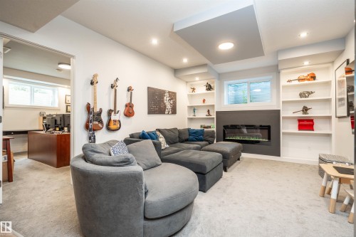 Bright entertainment area featuring an electric fireplace with a dark accent wall, built-in shelving, recessed lighting, and a light carpeted floor - 4714 Charles Bay Bay, Edmonton, AB 