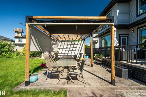 Outdoor patio featuring a pergola with a retractable shade cover, an expansive lawn, and a multi-level deck with black railings - 4714 Charles Bay Bay, Edmonton, AB 
