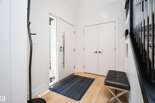 Foyer with wood-finish flooring, white walls, and a contemporary entry door featuring a long pull handle and smart lock - 4714 Charles Bay Bay, Edmonton, AB 