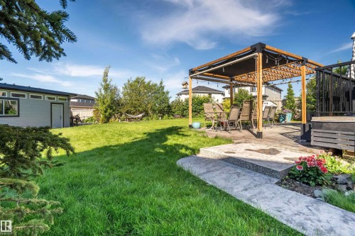 Expansive backyard featuring a large green space, a modern pergola on a concrete patio, a detached shed with horizontal siding, a black composite deck, and mature trees - 4714 Charles Bay, Edmonton, AB 