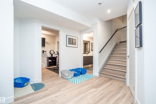 Light wood-finish flooring extending through a lower-level hallway with a staircase featuring a dark handrail and white risers - 4714 Charles Bay Bay, Edmonton, AB 