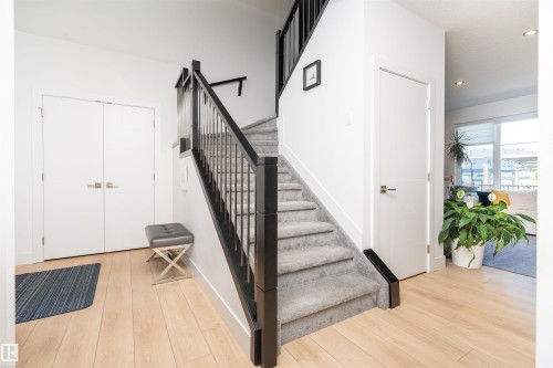 Entryway featuring wood-finish flooring, a carpeted staircase with a dark banister, white walls, and recessed lighting - 4714 Charles Bay Bay, Edmonton, AB 