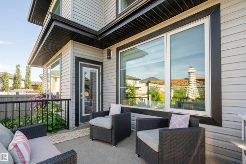 Outdoor concrete patio featuring a glass-paneled door, large windows, and a black metal railing - 4714 Charles Bay Bay, Edmonton, AB 