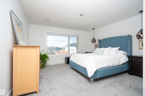 Spacious bedroom featuring light gray carpeting, recessed ceiling lighting, a large window, and pendant light fixtures - 4714 Charles Bay Bay, Edmonton, AB 