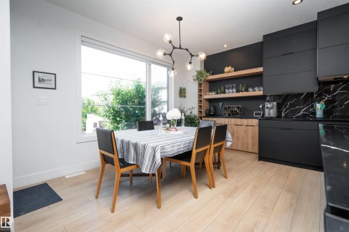 Dining area featuring light wood-finish flooring, a large window, and a modern black chandelier - 4714 Charles Bay Bay, Edmonton, AB 