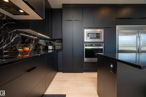 Modern kitchen featuring matte black cabinetry with integrated stainless steel appliances, black countertops, and a striking black marble-look backsplash - 4714 Charles Bay Bay, Edmonton, AB 