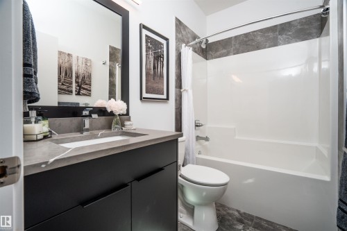 Contemporary bathroom featuring a dark vanity with an integrated rectangular sink, a stone-finish countertop, and a sleek rectangular mirror - 4714 Charles Bay Bay, Edmonton, AB 