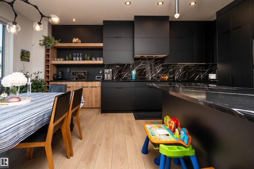 Open-concept kitchen featuring black flat-panel cabinetry, a black and white veined backsplash, and a large central island with a matching countertop - 4714 Charles Bay Bay, Edmonton, AB 