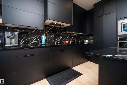 Modern kitchen featuring matte black cabinetry, black countertops with white veining, and a complementary black veined backsplash - 4714 Charles Bay Bay, Edmonton, AB 