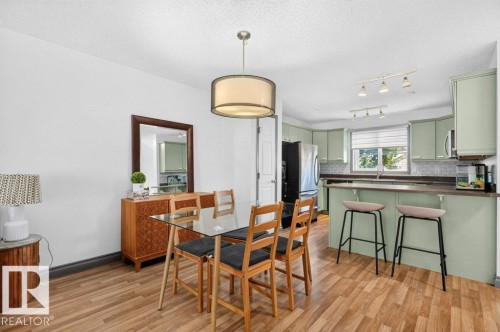 Open-concept dining area with wood-finish flooring, featuring a glass-top dining table, drum pendant lighting, and a mirrored accent piece - 21320 90 Avenue, Edmonton, AB 