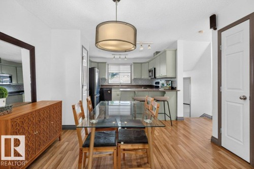 Open-concept dining area featuring wood-finish flooring, a contemporary drum pendant light, and direct access to the kitchen - 21320 90 Avenue, Edmonton, AB 