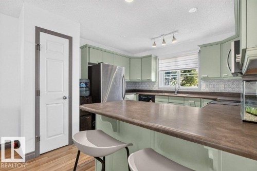 Kitchen featuring light green cabinetry, stainless steel appliances, and a breakfast bar with a solid surface countertop - 21320 90 Avenue, Edmonton, AB 