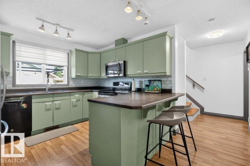 Kitchen featuring sage green cabinetry, a breakfast bar, stainless steel microwave, black dishwasher, and wood-finish flooring - 21320 90 Avenue, Edmonton, AB 