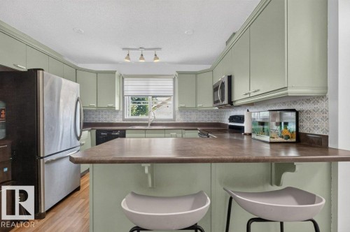 Kitchen featuring light green cabinetry, a patterned tile backsplash, stainless steel refrigerator, built-in microwave, and wood-finish flooring - 21320 90 Avenue, Edmonton, AB 