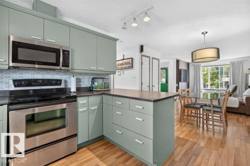 Kitchen featuring sage-toned cabinetry, stainless steel appliances, a patterned backsplash, and wood-finish flooring - 21320 90 Avenue, Edmonton, AB 