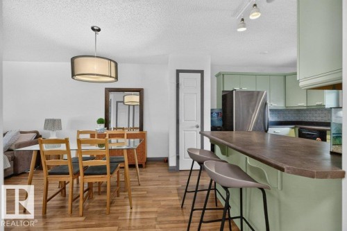 Open-concept living space featuring wood-finish flooring, a kitchen island with countertop seating, light green cabinetry, and stainless steel appliances - 21320 90 Avenue, Edmonton, AB 