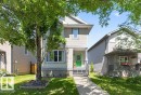 Two-story residence featuring light-colored siding with contrasting grey trim, a vibrant green front door, and a concrete pathway leading to the entrance - 21320 90 Avenue, Edmonton, AB 