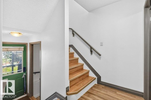 Entryway featuring wood-finish flooring, a green entry door with window, and a staircase with wood treads and a dark handrail - 21320 90 Avenue, Edmonton, AB 