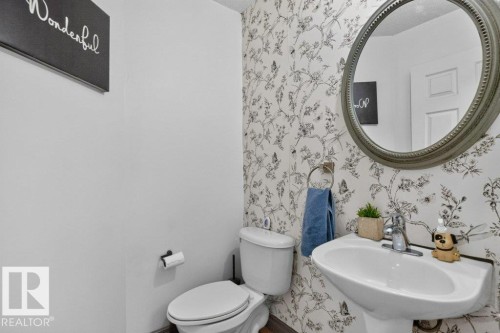 Powder room featuring a pedestal sink with a chrome faucet, a toilet, and a decorative round framed mirror - 21320 90 Avenue, Edmonton, AB 