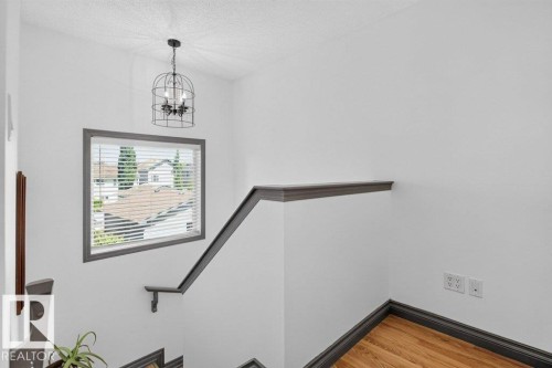 Staircase with wood-finish flooring, dark trim, and a window with blinds - 21320 90 Avenue, Edmonton, AB 
