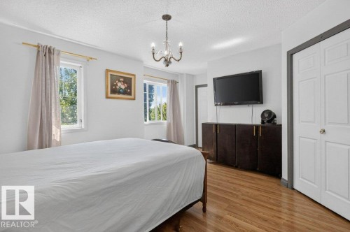 Bedroom featuring wood-finish flooring, a decorative chandelier, white walls, and two windows providing natural illumination - 21320 90 Avenue, Edmonton, AB 