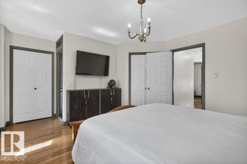 Bedroom featuring wood-finish flooring, a bi-fold closet door, a chandelier fixture, and a neutral wall color - 21320 90 Avenue, Edmonton, AB 